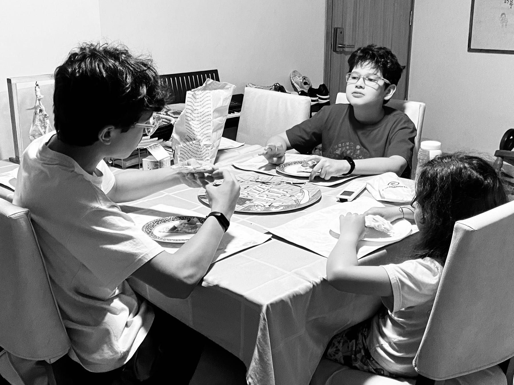 Tres hermanos conversan alrededor de la mesa mientras comen pizza